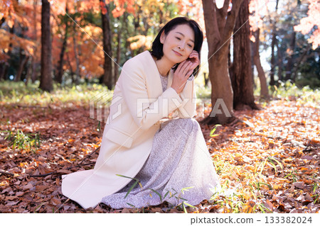 一位中年婦女在秋葉滿布的公園漫步 133382024