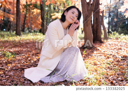 一位中年婦女在秋葉滿布的公園漫步 133382025
