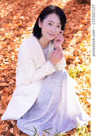 A middle-aged woman strolling through a park with autumn leaves 133382127