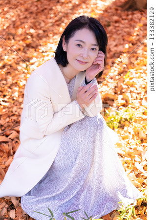 一位中年婦女在秋葉滿布的公園漫步 133382129