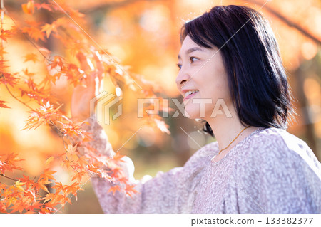 一位中年婦女在秋葉滿布的公園漫步 133382377