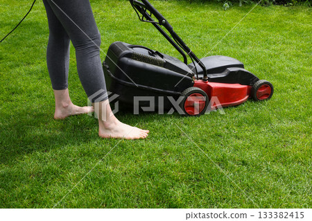 Woman mowing green grass lawn with mower Woman mowing green grass lawn with mower 133382415