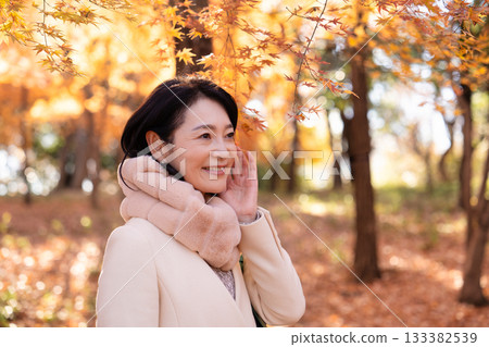 一位中年婦女在秋葉滿布的公園漫步 133382539