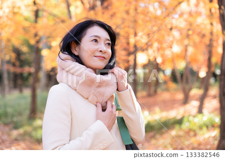 一位中年婦女在秋葉滿布的公園漫步 133382546