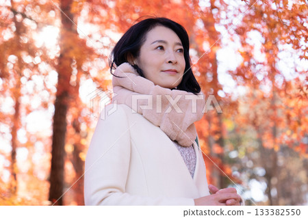 一位中年婦女在秋葉滿布的公園漫步 133382550
