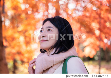 一位中年婦女在秋葉滿布的公園漫步 133382554