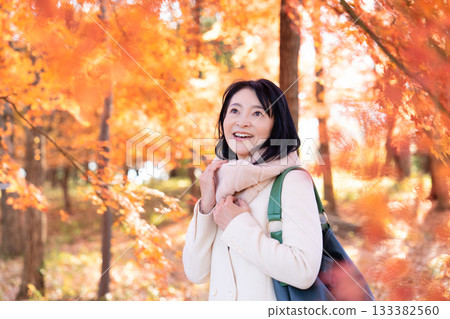 A middle-aged woman strolling through a park with autumn leaves A middle-aged woman strolling through a park with autumn leaves 133382560
