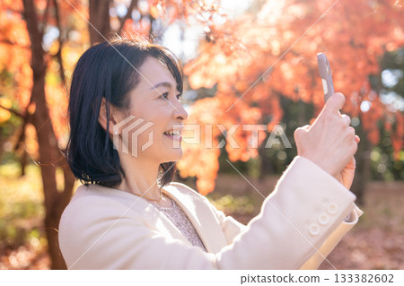 一位中年婦女在秋葉滿布的公園漫步 133382602