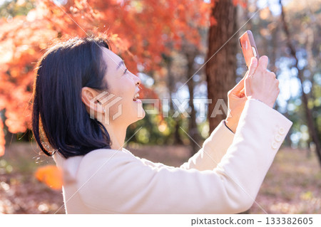 A middle-aged woman strolling through a park with autumn leaves 133382605