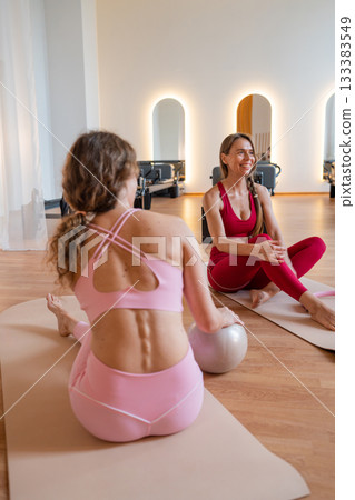 Pilates trainer conducts a conversation before the start of training, guiding her client through a pilates workout session on a reformer machine in a gym 133383549