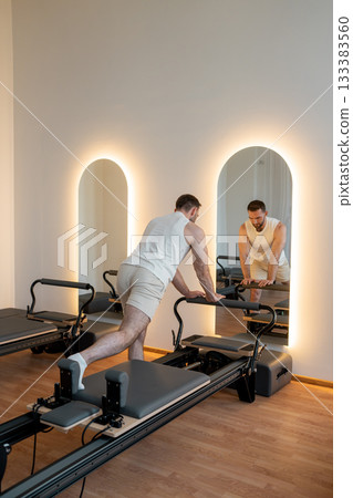 Man training pilates on the reformer bed. Reformer pilates studio machine for fitness workouts in gym. Fit, healthy and strong authentical body. Fitness concept 133383560