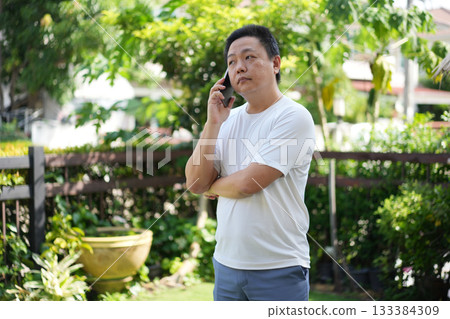Thoughtful Call, a man listens quietly to a phone conversation in the garden reflecting mindfulness focus and presence within daily life. Thoughtful Call, a man listens quietly to a phone conversation in the garden reflecting mindfulness focus and presence within daily life. 133384309