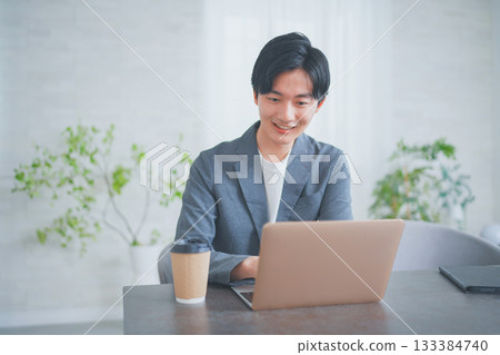 一位穿著休閒商務服裝的男士正在一邊喝咖啡一邊開會。 133384740