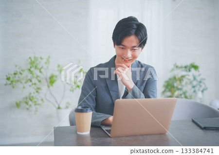 一位穿著休閒商務服裝的男士正在一邊喝咖啡一邊開會。 133384741