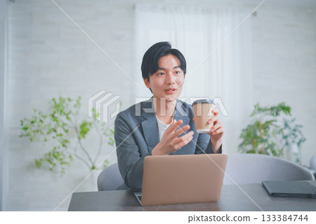 一位穿著休閒商務服裝的男士正在一邊喝咖啡一邊開會。 一位穿著休閒商務服裝的男士正在一邊喝咖啡一邊開會。 133384744
