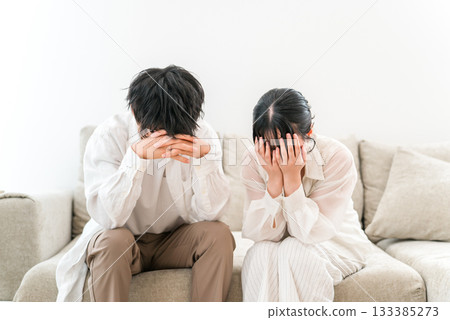 A couple sitting on the sofa and holding their heads in despair, couple (trouble, failure, shock) A couple sitting on the sofa and holding their heads in despair, couple (trouble, failure, shock) 133385273