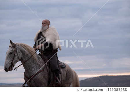 A majestic Viking chieftain on a dappled grey horse, clad in a fur cloak, surveys a desolate, mountainous landscape under a dramatic cloudy sky, exuding power and presence. A majestic Viking chieftain on a dappled grey horse, clad in a fur cloak, surveys a desolate, mountainous landscape under a dramatic cloudy sky, exuding power and presence. 133385388