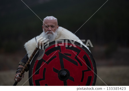 Viking warrior with axe standing on mountain cliff, wearing fur cloak and leather armor, overlooking dramatic landscape. Historical Nordic fighter Viking warrior with axe standing on mountain cliff, wearing fur cloak and leather armor, overlooking dramatic landscape. Historical Nordic fighter 133385423