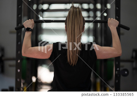 Weightlifting woman training indoors in a gym, focused on strength during an upper body workout session Weightlifting woman training indoors in a gym, focused on strength during an upper body workout session 133385565