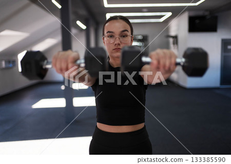 Woman exercises with dumbbells in modern gym setting during daylight hours 133385590