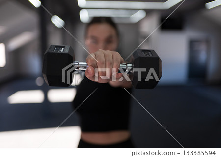 Fitness enthusiast working out with dumbbells in a modern gym setting during daytime 133385594