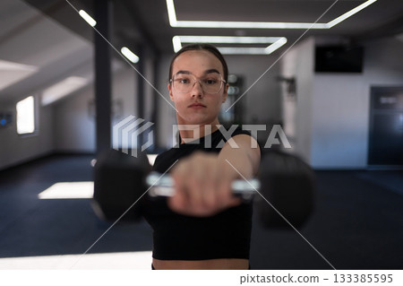 Young woman lifting dumbbell in modern fitness center during a workout session focusing on strength training and exercise 133385595
