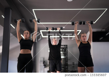 Women lifting weights in a modern gym during a fitness class 133385607