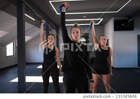 Group workout session featuring women lifting weights in a modern gym setting during daytime 133385608