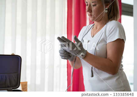 Professional female therapist wearing gloves and preparing equipment while a man lies on a massage table covered with a towel. Spa and wellness treatment concept highlighting relaxation, health care Professional female therapist wearing gloves and preparing equipment while a man lies on a massage table covered with a towel. Spa and wellness treatment concept highlighting relaxation, health care 133385648