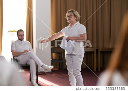 Instructor holding notes and pen while teaching massage therapy class to students, professional training and education in wellness and rehabilitation. Instructor holding notes and pen while teaching massage therapy class to students, professional training and education in wellness and rehabilitation. 133385663