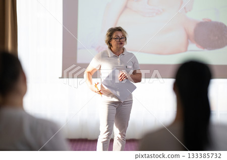 Instructor holding notes and pen while teaching massage therapy class to students, professional training and education in wellness and rehabilitation. 133385732