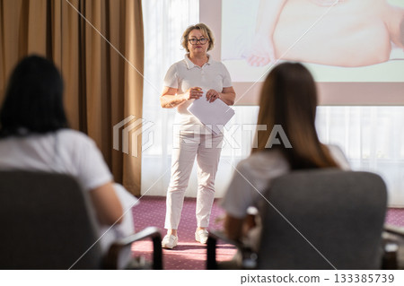 Instructor holding notes and pen while teaching massage therapy class to students, professional training and education in wellness and rehabilitation. 133385739