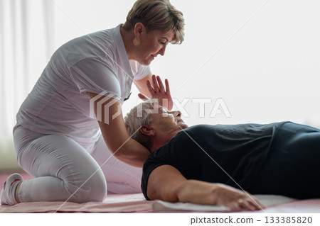 Close up of a physiotherapist holding the head and neck of an older woman lying on a mat during a rehabilitation session. Physiotherapy treatment concept focusing on pain relief, mobility improvement 133385820
