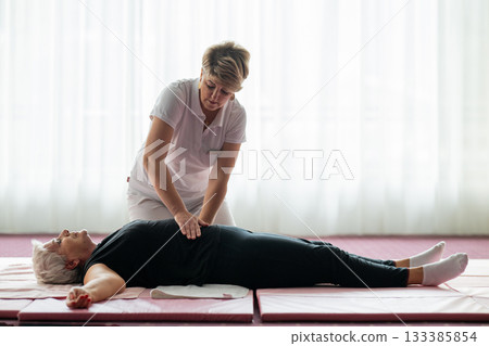 Professional female physiotherapist assisting an older woman lying on a mat during a therapeutic rehabilitation session. Wellness and physiotherapy concept highlighting recovery, mobility, pain relief Professional female physiotherapist assisting an older woman lying on a mat during a therapeutic rehabilitation session. Wellness and physiotherapy concept highlighting recovery, mobility, pain relief 133385854