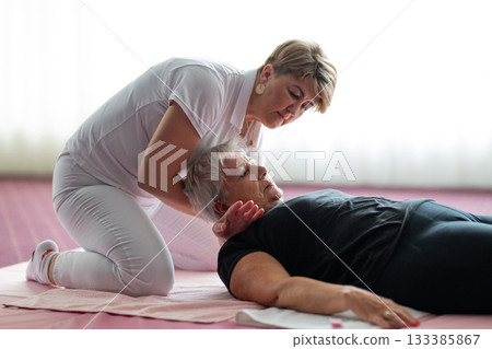 Close up of a physiotherapist holding the head and neck of an older woman lying on a mat during a rehabilitation session. Physiotherapy treatment concept focusing on pain relief, mobility improvement Close up of a physiotherapist holding the head and neck of an older woman lying on a mat during a rehabilitation session. Physiotherapy treatment concept focusing on pain relief, mobility improvement 133385867