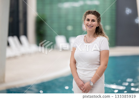 Portrait of a young female wellness coach smiling confidently at an indoor swimming pool, symbolizing health, fitness, and professional guidance. 133385919