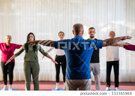 Instructor leading a diverse group of people during a fitness training session with stretching exercises on mats in a bright wellness center Instructor leading a diverse group of people during a fitness training session with stretching exercises on mats in a bright wellness center 133385968