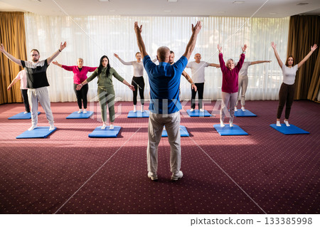 Instructor leading a diverse group of people during a fitness training session with stretching exercises on mats in a bright wellness center Instructor leading a diverse group of people during a fitness training session with stretching exercises on mats in a bright wellness center 133385998