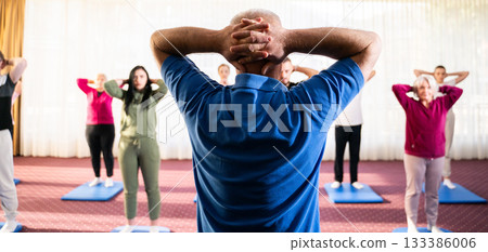 Instructor leading a diverse group of people during a fitness training session with stretching exercises on mats in a bright wellness center 133386006