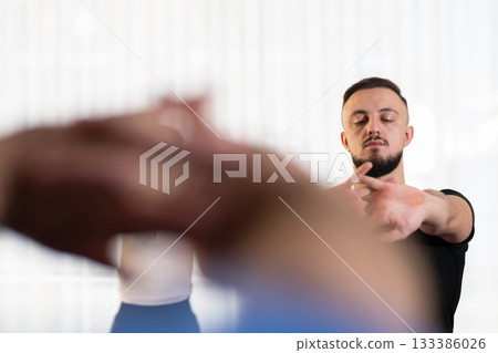 Man stretching his arms forward during a fitness or rehabilitation class indoors. Concept of focus, mindfulness, health, and active lifestyle. Man stretching his arms forward during a fitness or rehabilitation class indoors. Concept of focus, mindfulness, health, and active lifestyle. 133386026