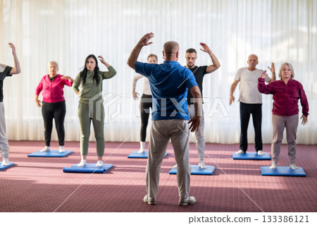 Instructor leading a diverse group of people during a fitness training session with stretching exercises on mats in a bright wellness center 133386121