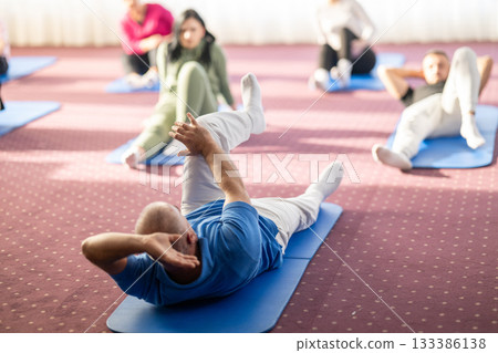 Instructor leading a diverse group of people during a fitness training session with stretching exercises on mats in a bright wellness center Instructor leading a diverse group of people during a fitness training session with stretching exercises on mats in a bright wellness center 133386138