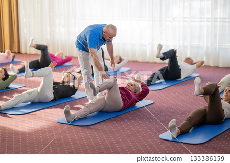 Instructor leading a diverse group of people during a fitness training session with stretching exercises on mats in a bright wellness center 133386159