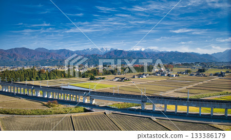 A view of the Hokuriku Shinkansen line near the viaduct running through Nyuzen Town, Toyama Prefecture, with the Northern Alps in the background 133386179