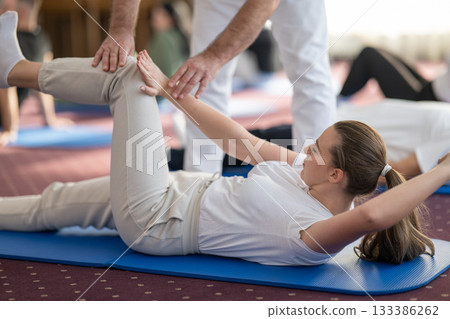 Instructor Helping Woman Stretch During Pilates or Rehabilitation Class 133386262