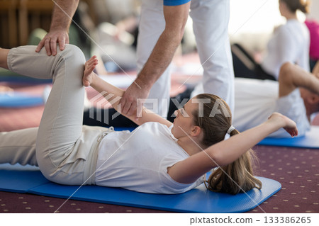 Instructor Helping Woman Stretch During Pilates or Rehabilitation Class 133386265