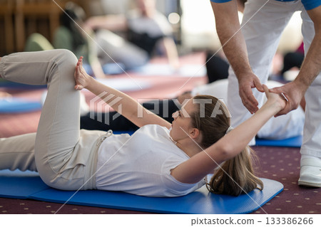 Instructor Helping Woman Stretch During Pilates or Rehabilitation Class 133386266