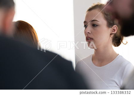 Portrait of a young woman attentively participating in a group wellness or mindfulness session indoors. Concept of concentration, self awareness, and mental clarity. 133386332
