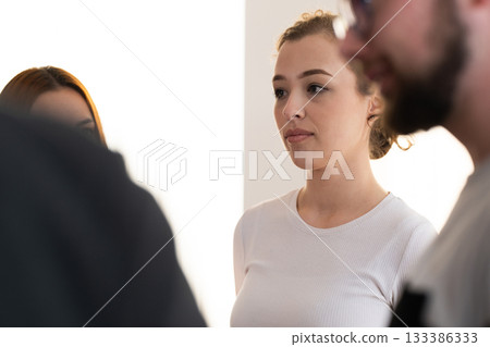 Portrait of a young woman attentively participating in a group wellness or mindfulness session indoors. Concept of concentration, self awareness, and mental clarity. 133386333