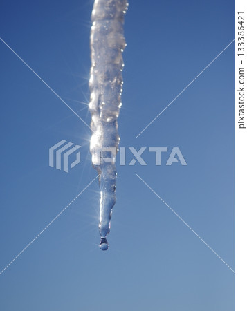 A long icicle hanging from a blue sky 133386421